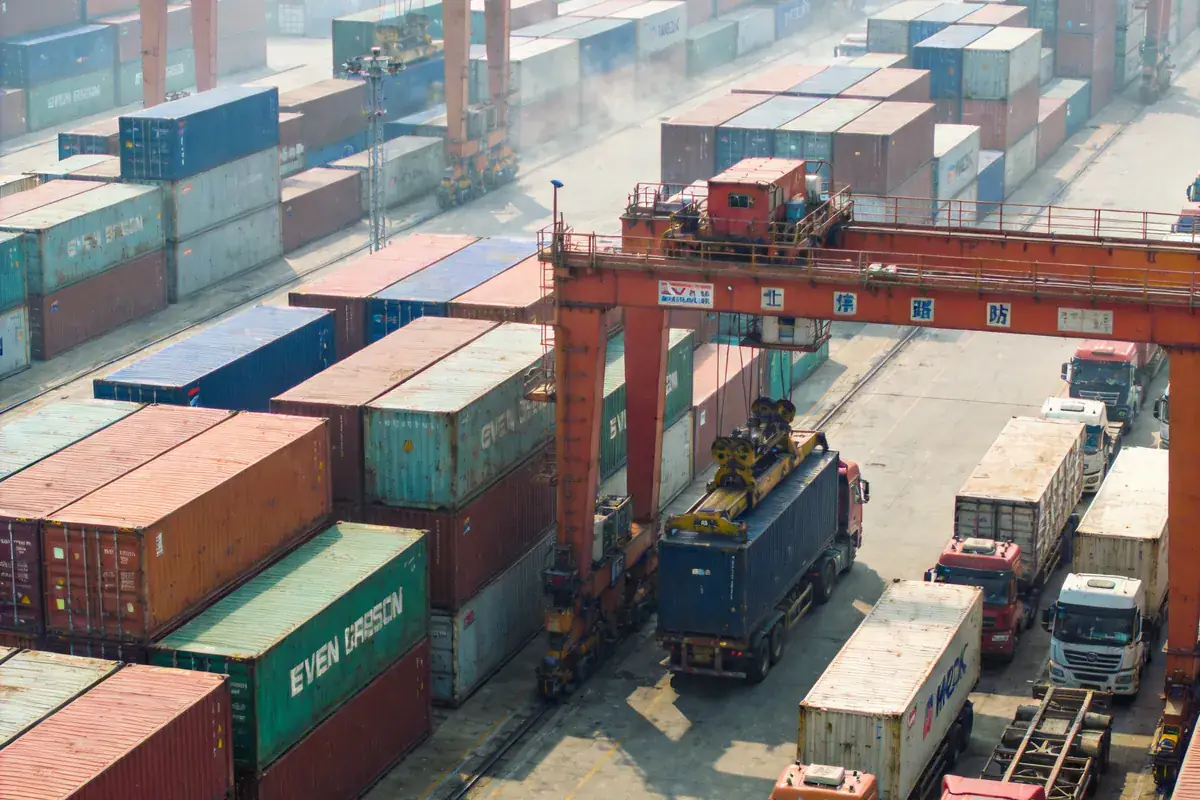Yiwu port container terminal in China, rows of stacked containers and gantry cranes loading trucks